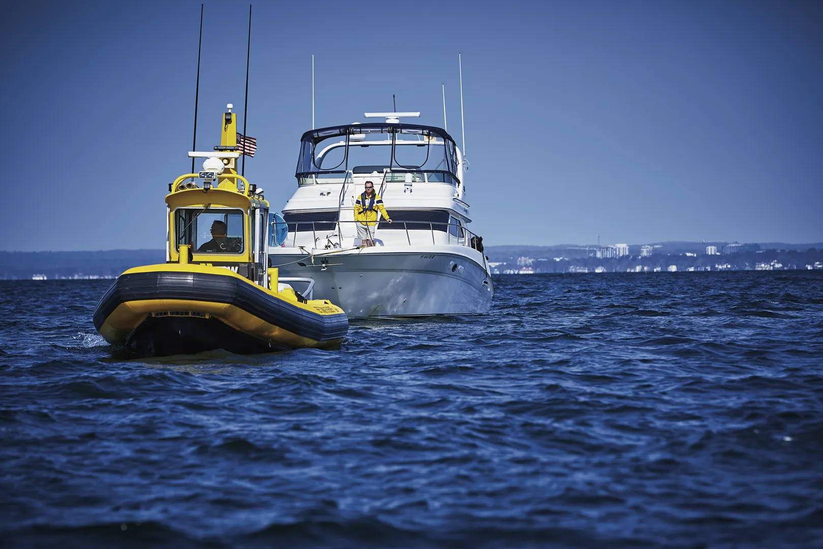 Man in yellow jacket on yacht being towed by sea tow.